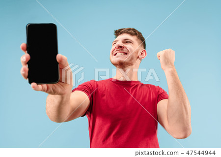Young handsome man showing smartphone screen isolated on blue background in shock with a surprise 47544944