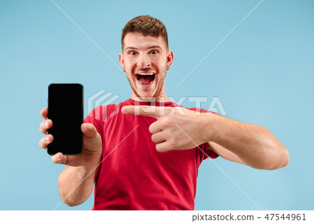 Young handsome man showing smartphone screen isolated on blue background in shock with a surprise 47544961