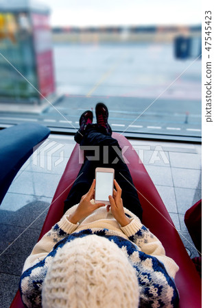Girl using phone while waiting at the airport Girl using phone while waiting at the airport 47545423
