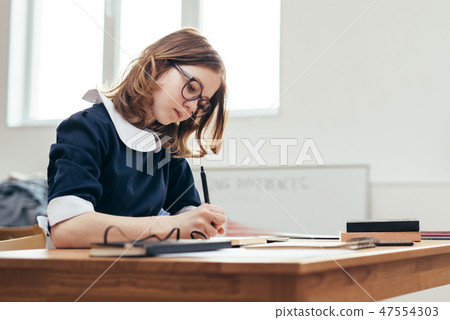 School Girl writes in a notebook sitting at table Classwork, homework 47554303