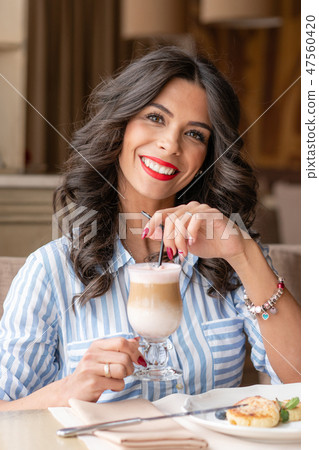 Beautiful young woman enjoying coffee cappuccino or latte in a glass cup with foam. Light breakfast 47560420