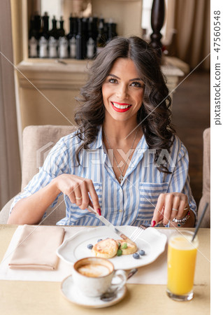 Beautiful young woman cuts pancakes with a knife, enjoying coffee cappuccino or latte in a glass cup 47560548