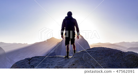 Man on a cliff with view of sun and mountains Man on a cliff with view of sun and mountains 47562091