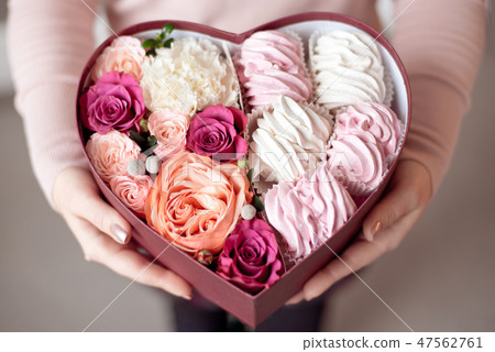 A bouquet of flowers and marshmallows in a gift box of heart in female hands. Congratulatory concept A bouquet of flowers and marshmallows in a gift box of heart in female hands. Congratulatory concept 47562761