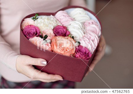 A bouquet of flowers and marshmallows in a gift box of heart in female hands. Congratulatory concept 47562765
