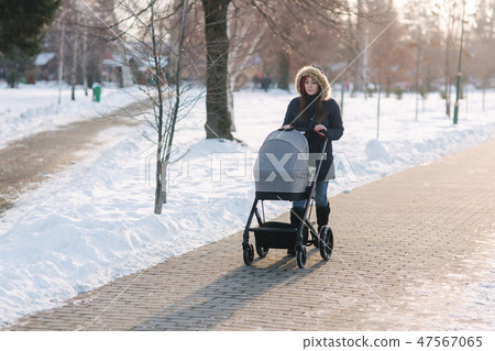 Beautiful mother walking in the park with her little baby in stoller. Woman dressed in blue jaket Beautiful mother walking in the park with her little baby in stoller. Woman dressed in blue jaket 47567065
