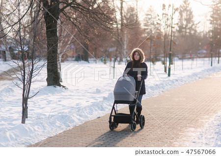 Beautiful mother walking in the park with her little baby in stoller. Woman dressed in blue jaket Beautiful mother walking in the park with her little baby in stoller. Woman dressed in blue jaket 47567066