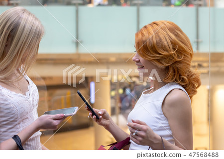 Pretty female friends exchanging phone numbers at mall shop 47568488