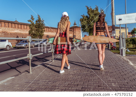 Two girls walking on foot, women girlfriends in summer in the city on the road. With a longboard 47570152