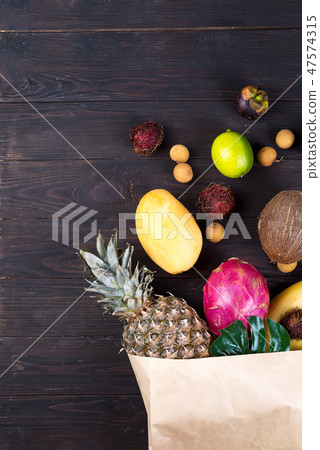 Paper bag of different healthy tropical fruits on dark wooden background. Top view. Paper bag of different healthy tropical fruits on dark wooden background. Top view. 47574315