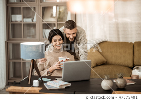 Curious bearded man in grey cardigan looking on the screen 47575491