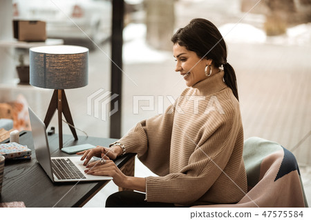 Contented beautiful lady working with laptop while sitting in office armchair Contented beautiful lady working with laptop while sitting in office armchair 47575584