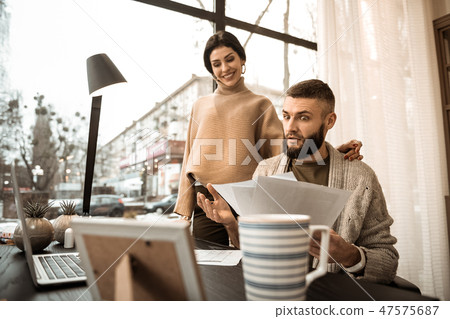Shocked bearded guy carrying papers and showing them to his wife Shocked bearded guy carrying papers and showing them to his wife 47575687