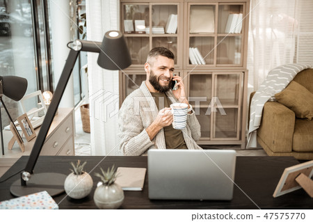 Cheerful positive man talking on mobile phone and drinking hot tea 47575770