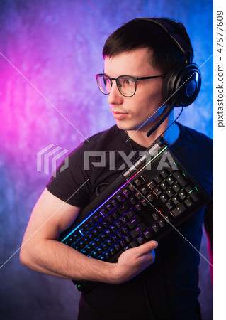 Computer nerd with keyboard over colorful pink and blue neon lit wall 47577609