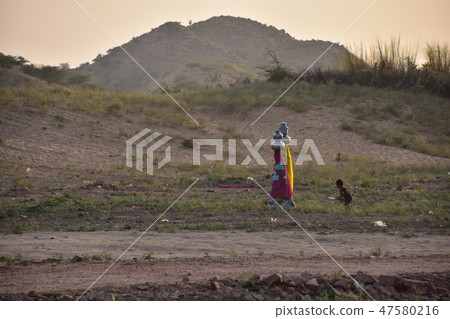 An Indian woman carrying a Psycq water bottle at dusk of Rajasthan in India and a boy to help 47580216