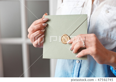 Close-up woman with slim body holding in hands the invitation card gray-green color square shape Close-up woman with slim body holding in hands the invitation card gray-green color square shape 47592745