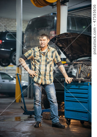 Car repair service. Brutal serious mechanic man stands next to the tool case Car repair service. Brutal serious mechanic man stands next to the tool case 47593656