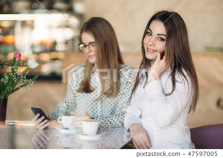Two girls sitting in a cafe drinking cappuccino and using smartphone. Modern girl Two girls sitting in a cafe drinking cappuccino and using smartphone. Modern girl 47597005