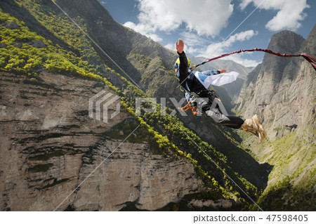 A man in a helmet jumps ropeup with an empty flag in the mountains. Extreme sports. Leisure A man in a helmet jumps ropeup with an empty flag in the mountains. Extreme sports. Leisure 47598405