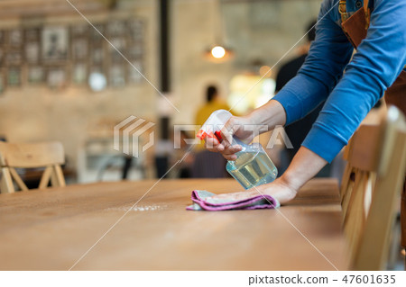 Waiter cleaning table with spray disinfectant  47601635