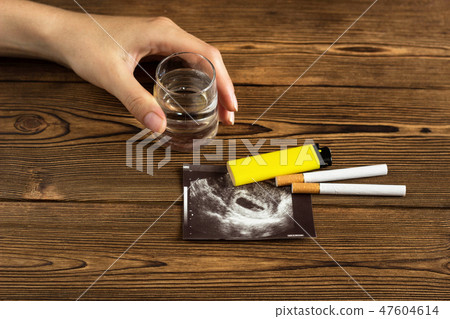 A woman's hand holds a glass of alcohol, next to it is a photograph of the uzi pregnancy and 47604614
