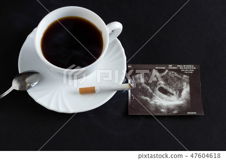 A cup of coffee and a burning cigarette, next to it there is a photograph of the uzi of pregnancy A cup of coffee and a burning cigarette, next to it there is a photograph of the uzi of pregnancy 47604618