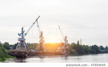 Port cranes with a bucket on the river bank, extraction of river sand, the sun Port cranes with a bucket on the river bank, extraction of river sand, the sun 47604649