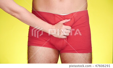 man in red boxers on a yellow background. a female hand caresses the thighs of a man. close-up man in red boxers on a yellow background. a female hand caresses the thighs of a man. close-up 47606291