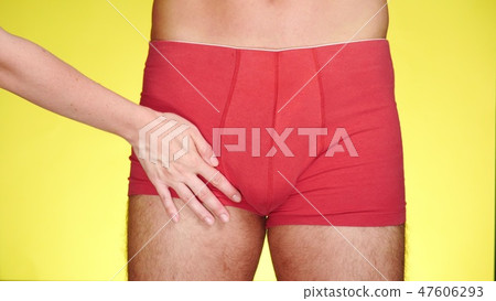 man in red boxers on a yellow background. a female hand caresses the thighs of a man. close-up 47606293