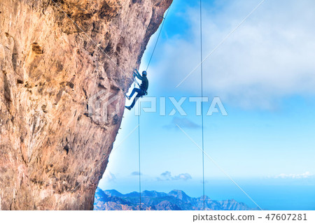 Rock climber climbing up overhanging cliff Rock climber climbing up overhanging cliff 47607281