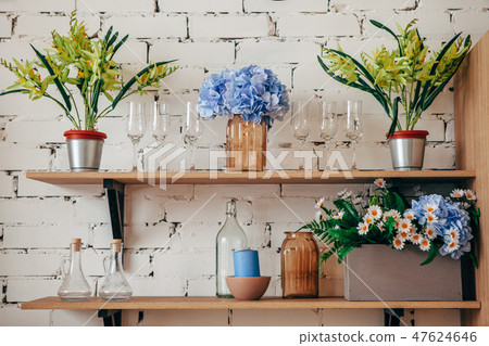 Kitchen interior: bottles, flower pots, flowers, glasses on the shelves. Cozy home interior. 47624646