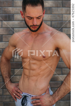 Young athlete posing with a torso for photography on a brick wall background. Bodybuilder, athlete 47625892
