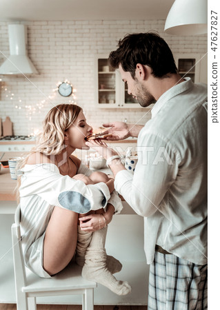 Brunette bearded man in a white shirt giving a sandwich to his wife Brunette bearded man in a white shirt giving a sandwich to his wife 47627827