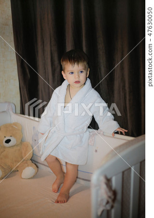 A little boy stands on the bed and poses in a home robe 47630050