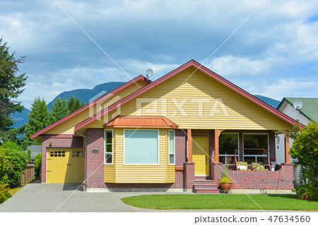 Yellow residential house with accurate lawn and concrete driveway to the garage 47634560