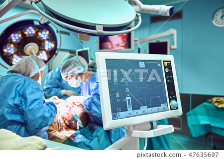 Monitoring patient's vital sign in operating room in focus. On backgdound blured surgery of Chin Monitoring patient's vital sign in operating room in focus. On backgdound blured surgery of Chin 47635697