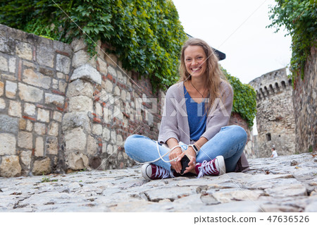 Pretty tourist girl sitting on empty street of historic city in hot summer day. Young woman posing 47636526