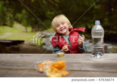 Little boy is eating snacks during picnic Little boy is eating snacks during picnic 47636674