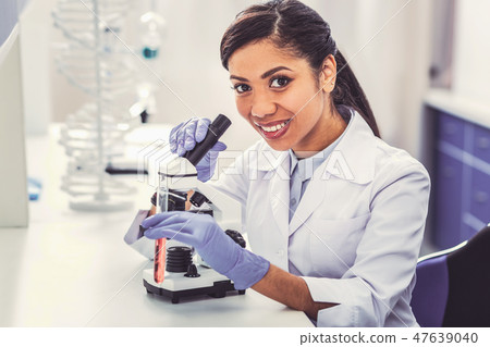 Smiling appealing chemist looking into microscope 47639040