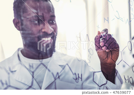 Skillful young chemical assistant standing near glass board Skillful young chemical assistant standing near glass board 47639077
