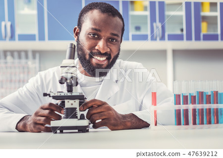 Black-eyed man working as chemist sitting near microscope 47639212