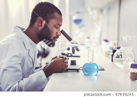 Young chemical practitioner looking into microscope 47639243