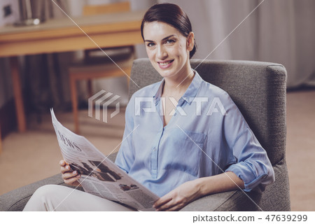 Delighted lady relaxing with a newspaper Delighted lady relaxing with a newspaper 47639299