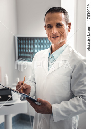 Wrinkled chiropractor wearing white uniform preparing health record Wrinkled chiropractor wearing white uniform preparing health record 47639629