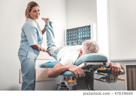 Chiropractor in blue uniform checking legs of elderly man 47639689