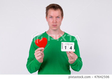 Young handsome man holding calendar block and heart ready for Valentine's day Young handsome man holding calendar block and heart ready for Valentine's day 47642506
