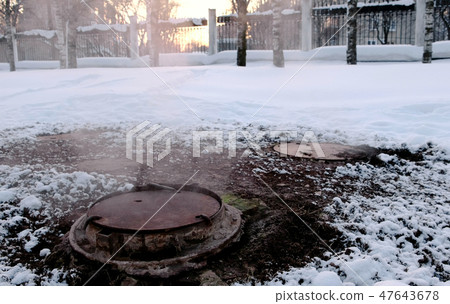 Close-up steam is from sanitary sewer cover in snow in winter park. Melted snow around. Close-up steam is from sanitary sewer cover in snow in winter park. Melted snow around. 47643678