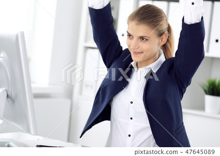 Modern business woman or confident female accountant in office with arms raised represents success 47645089