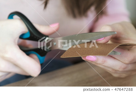 Close-up of the woman's hands cut out a piece of leather, preparing for sewing, cutting. Close-up of the woman's hands cut out a piece of leather, preparing for sewing, cutting. 47647288
